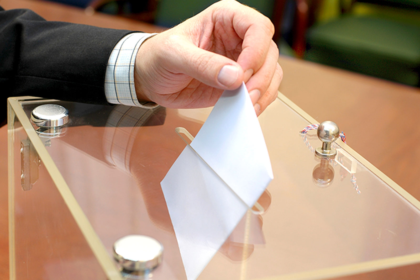 Hand steckt einen Wahlzettel in eine Wahlurne